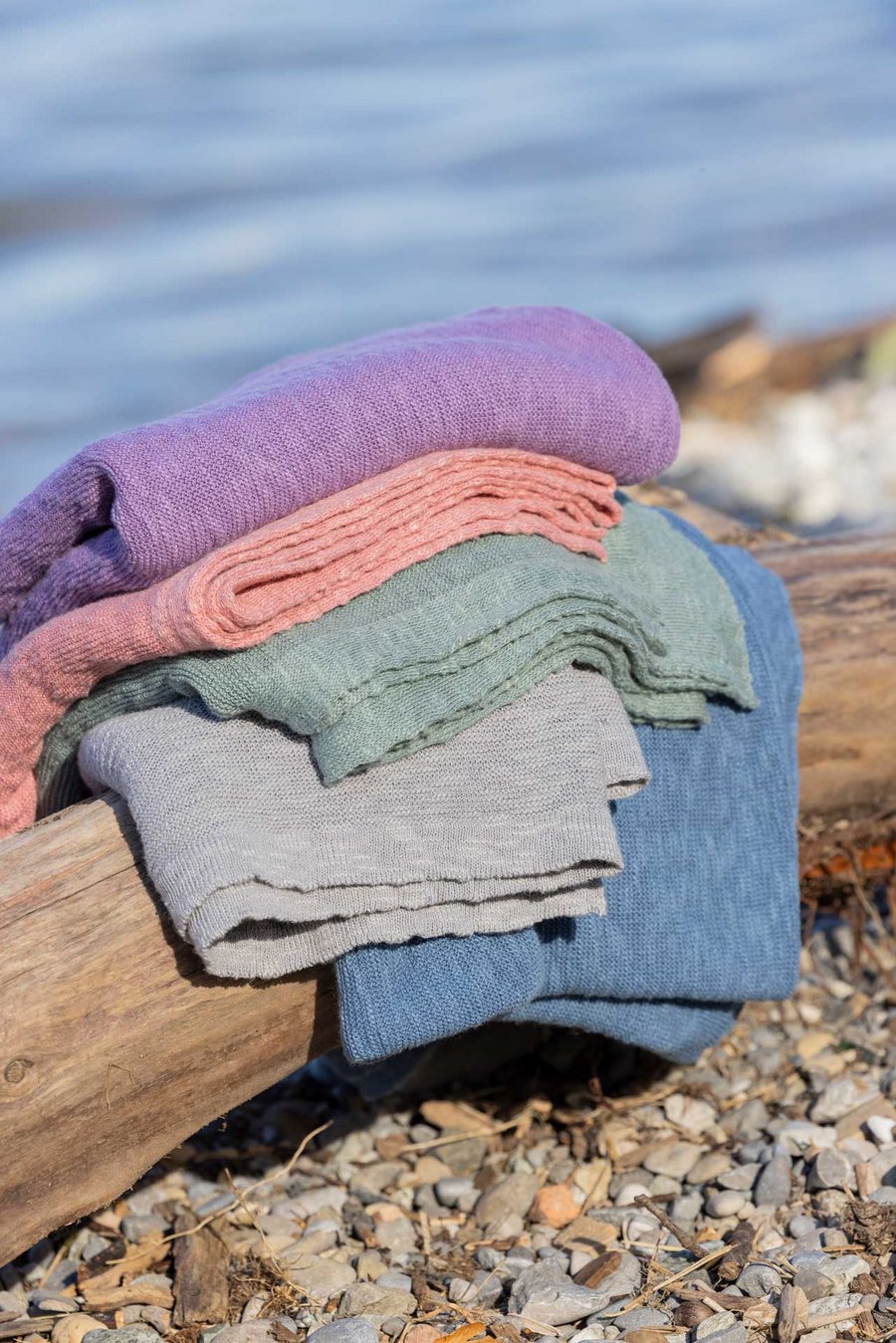 Gestapelte disana Leinen-Decken in Flieder, Softpink, Jade, Grau, Taubenblau auf einem verwitterten Holzstamm am Seeufer